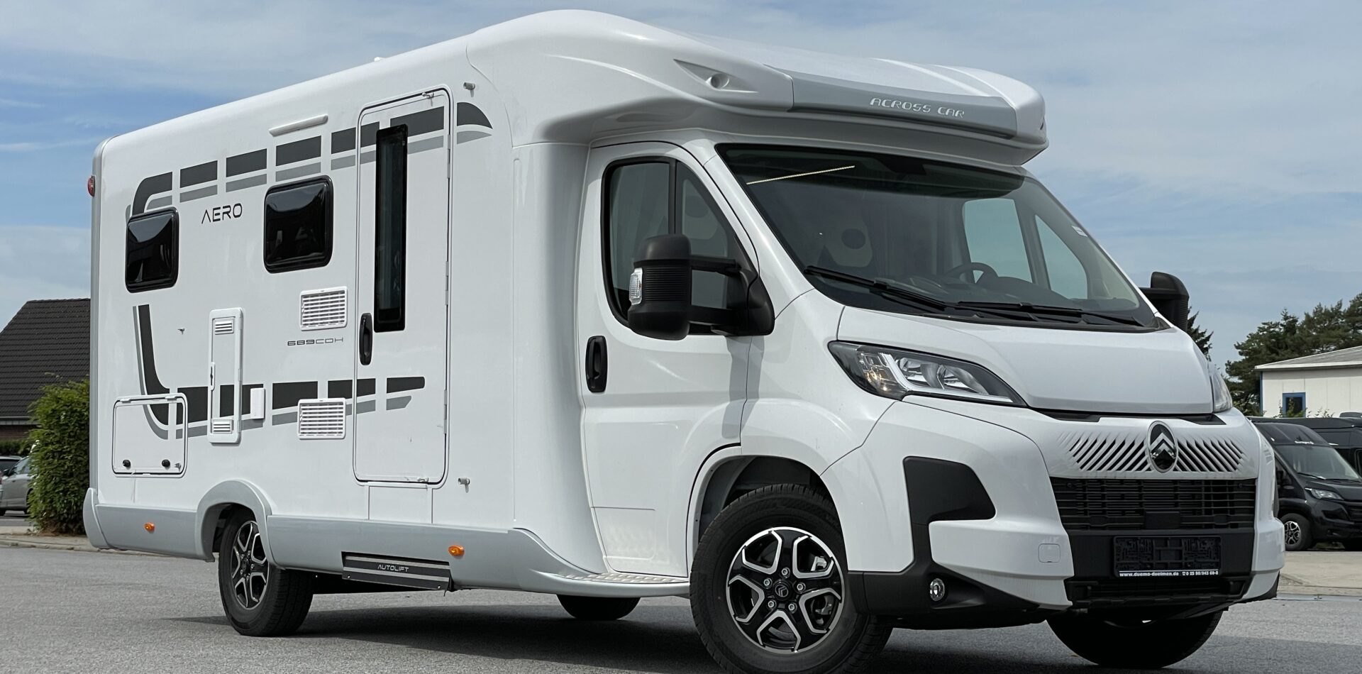 Weißes ACROSS Aero Wohnmobil mit integriertem Rollstuhl-Liftsystem für barrierefreies Reisen, aufgenommen auf einem Außengelände in Front-Seitenansicht.